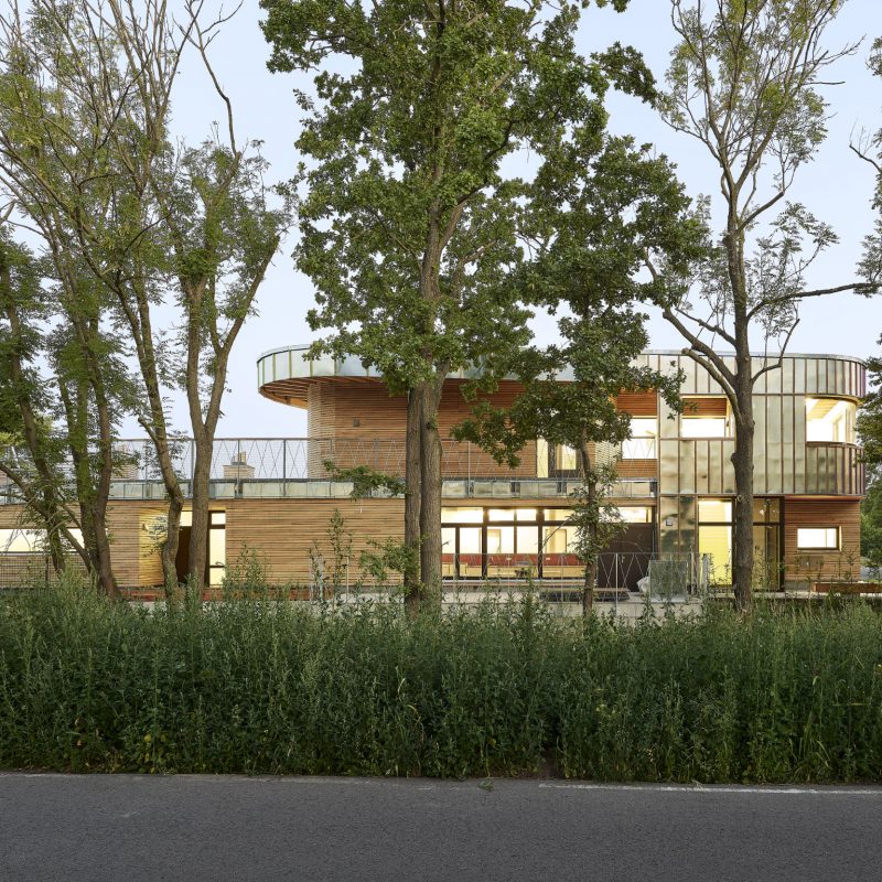 Kita mit Holz- und Metallfassade hinter Bäumen